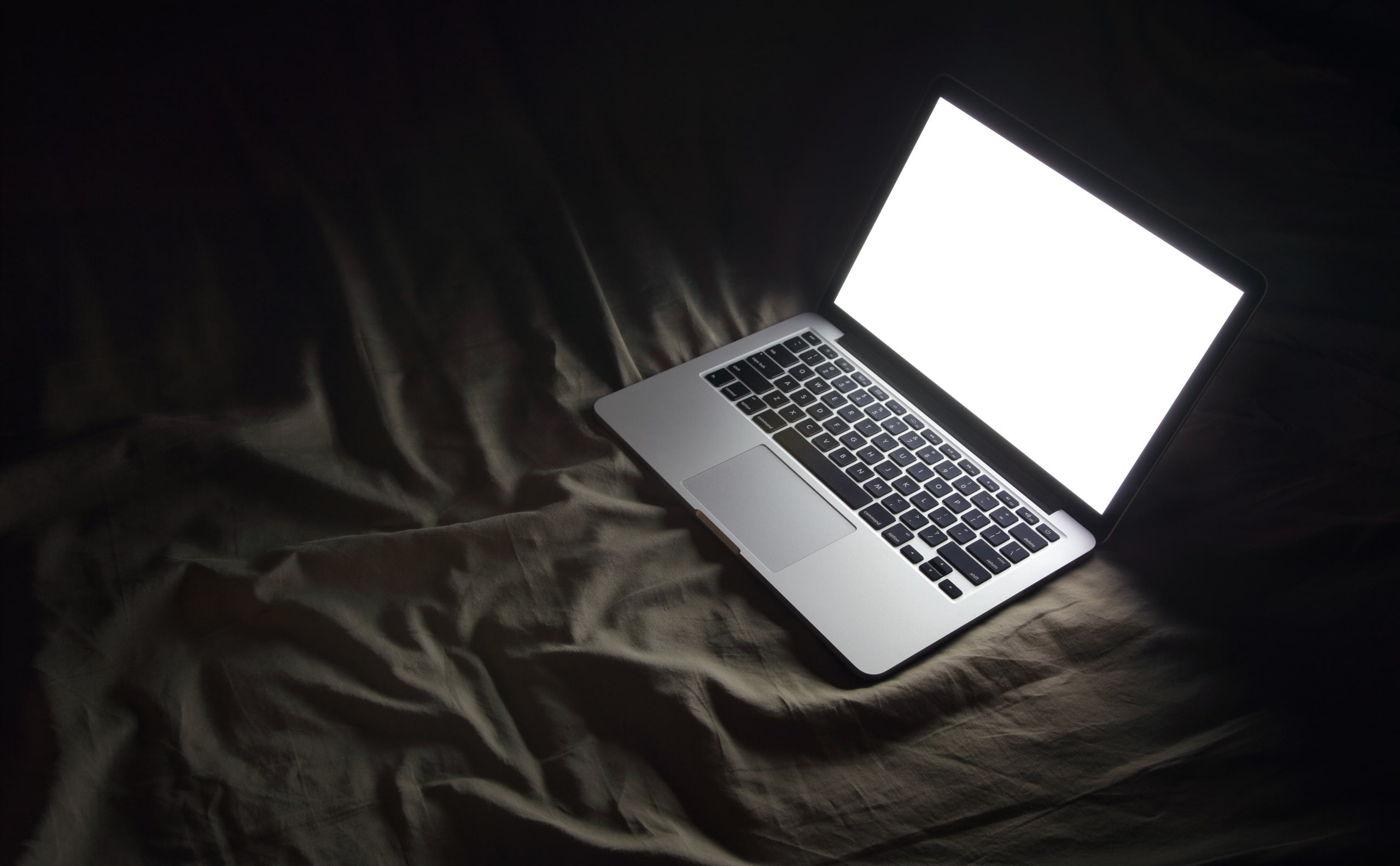 open laptop on dark bed